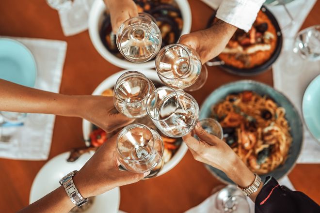 Hands holding glasses, with food on table