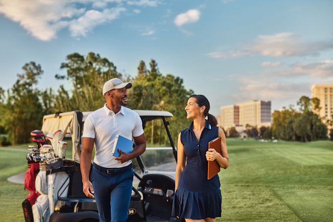Man and woman walking across golf course with bugging in background