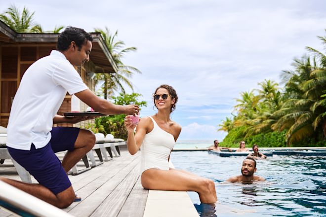 Groupe de personnes se relaxant dans la piscine, tandis que le membre du personnel sert une boisson à une femme