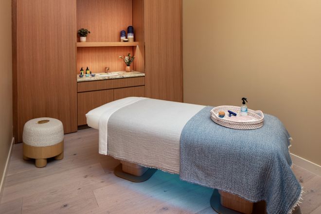 Masaj masası, ortam aydınlatması ve dokuma tepsisinde oturan ürünlerin bulunduğu spa bakım odası.