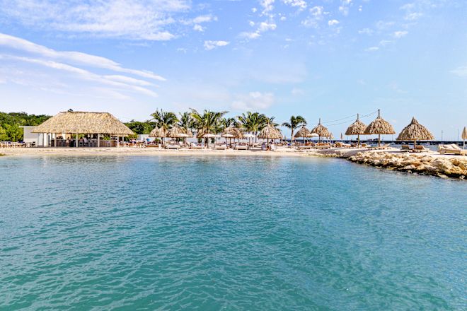 Außenansicht mit Blick auf einen Strand und Lounge-Sessel unter gestrohten Sonnenschirmen
