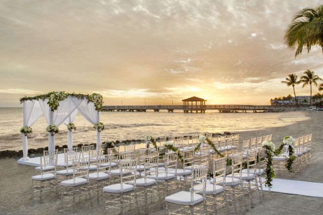 beach wedding ceremony set up, white chairs, gazebo, at sunset