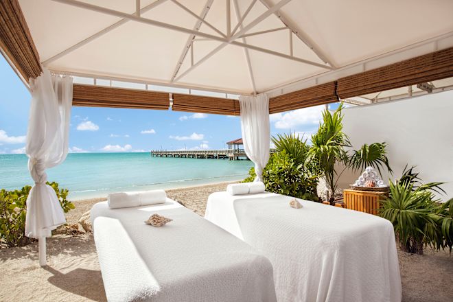 Two massage tables set up under a shelter with azure sea and a jetty in the background.