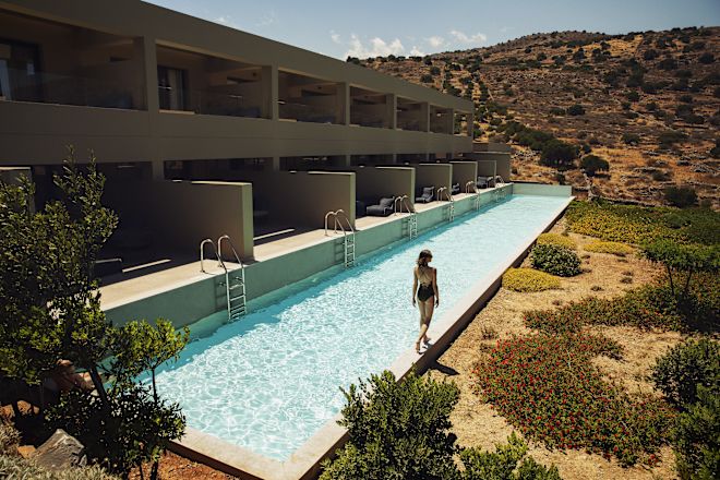 A long, narrow swimming pool with individual room access, set in a hilly landscape.