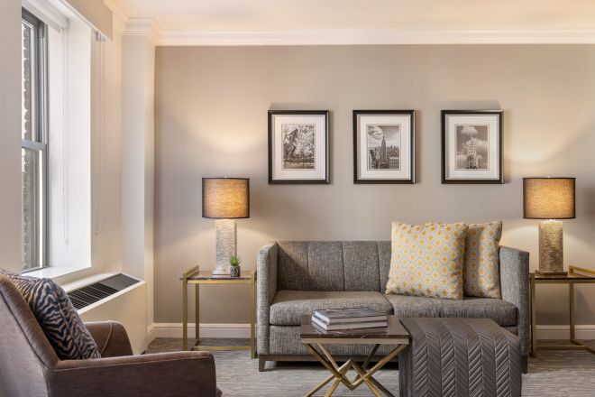 Zona de lounge a apartamentului Junior include o canapea cu perne decorative galbene și albe, mese de la capăt cu lămpi, o masă mică, otoman și scaun.