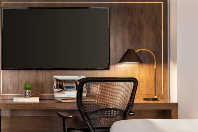 Junior suite work desk with a lamp, ergonomic chair and a wall-mounted TV.