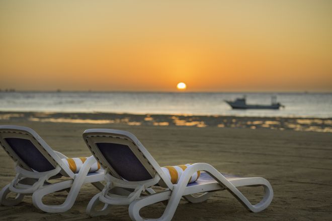 Beach with Deck Chairs and View of Sunrise above Ocean with Boat