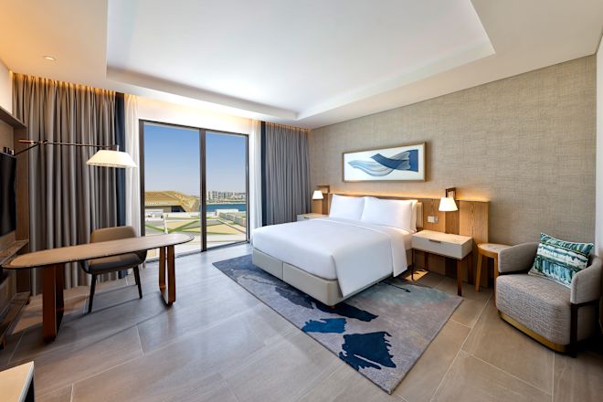 大きなベッド、デスク、アームチェア、大きな窓を備えたアクセシブルゲストルーム