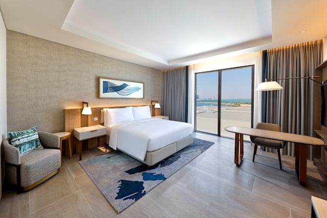 大きなベッド、ワークデスク、アームチェアを備えたウォータービューのアクセシブルルーム