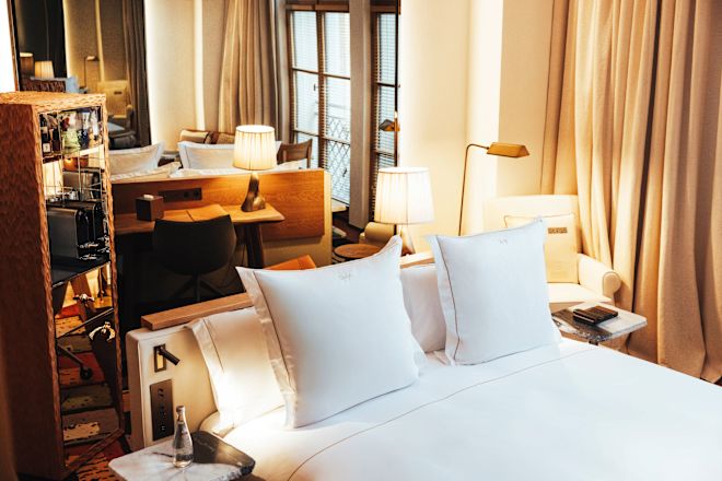 Tempat tidur dalam kamar dengan dua bantal, lampu, dan meja samping