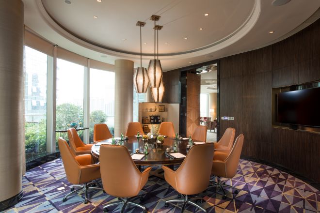 Boardroom with large round table, chairs, TV, and floor-to-ceiling windows with outdoor view