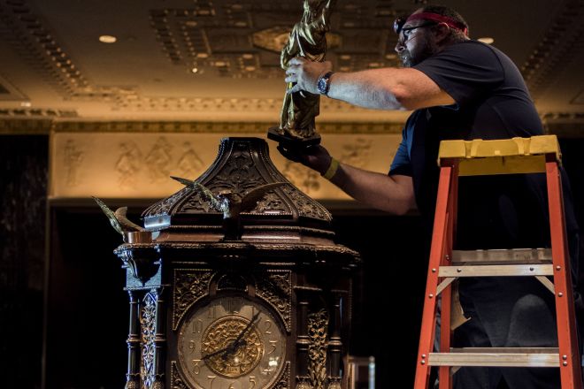 man on a ladder adding the statue of liberty replica to the top of the Waldorf Astoria lobby clock