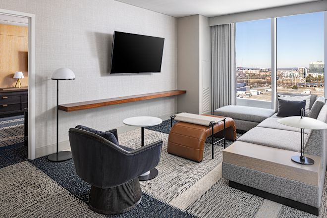 Brightly-lit hotel room living area with couch, chaise, and TV