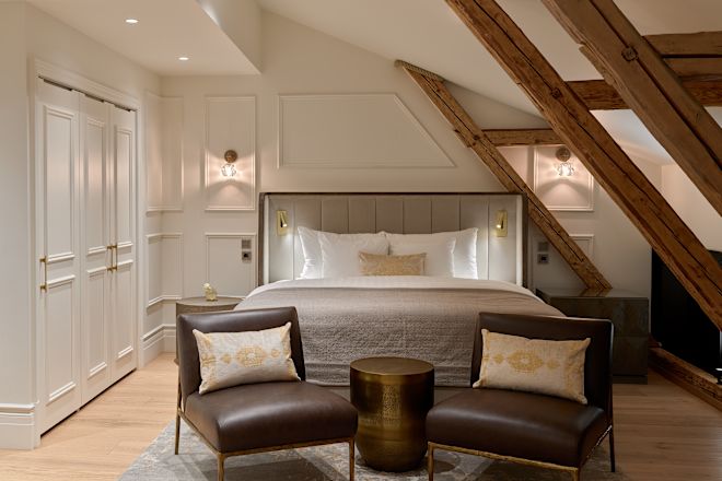 غرفة نوم بها سرير كينج، ومقعدين، وسقف منخفض بزاوية مع عوارض خشبية مكشوفة