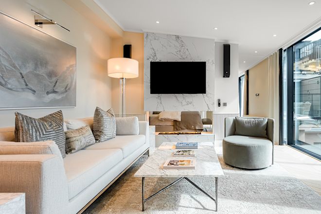 غرفة معيشة بها أريكة، ومقعد بذراعين، ومدفأة، وتلفزيون، وأبواب زجاجية منزلقة تؤدي إلى فناء