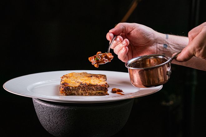 トライベッカ・マーケットのプレートにラザニアを1枚載せてフォークを握る手