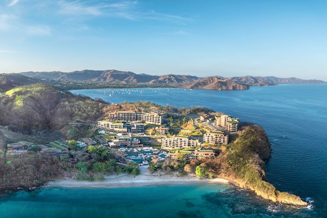 Drone shot of hotel exterior from a distance, showing surrounding ocean and coast
