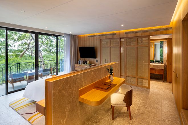 Schlafzimmer der Pacifico Suite, Schreibtisch, Bett, Fernseher, Fensterblick auf Balkon und Bäume