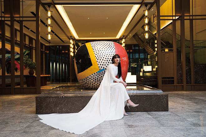 Bride in gown sitting in front of sculpture.