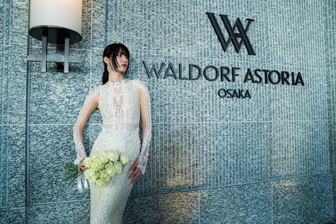 Bride in a modern wedding gown, with a white rose boquet in front of hotel signage.