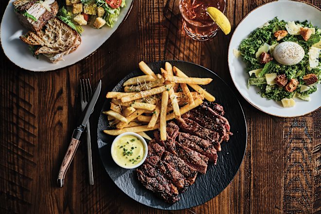 Carne cu sos și cartofi prăjiți pe o farfurie, salată și băuturi pe o masă la restaurantul cu pudră