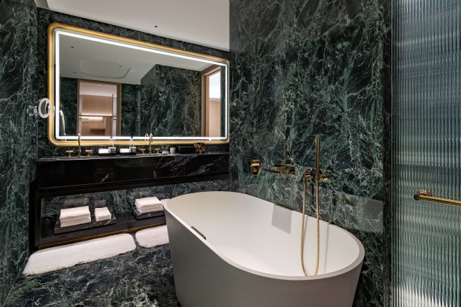 バスタブと照明付き鏡を備えたダブルシンクの洗面台エリアを備えたバスルーム