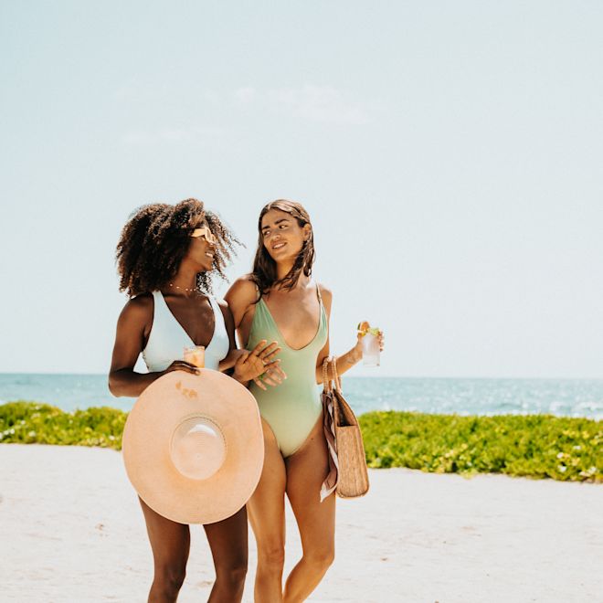 Two women walking along beach with drinks