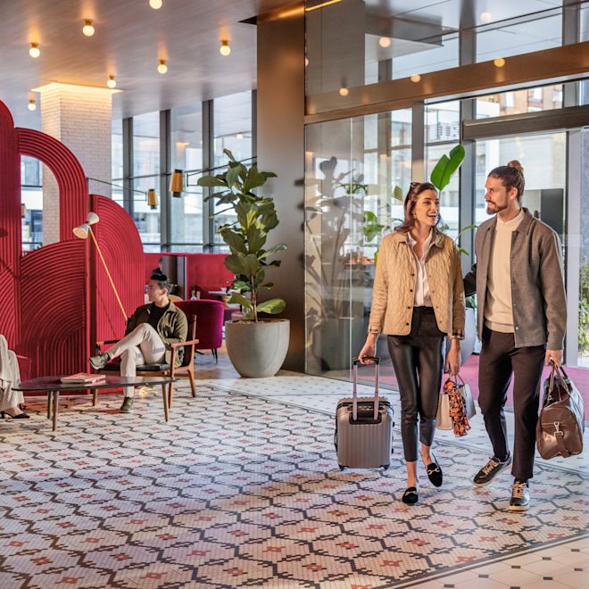 Hombre y mujer caminando por la entrada principal al lobby con equipaje