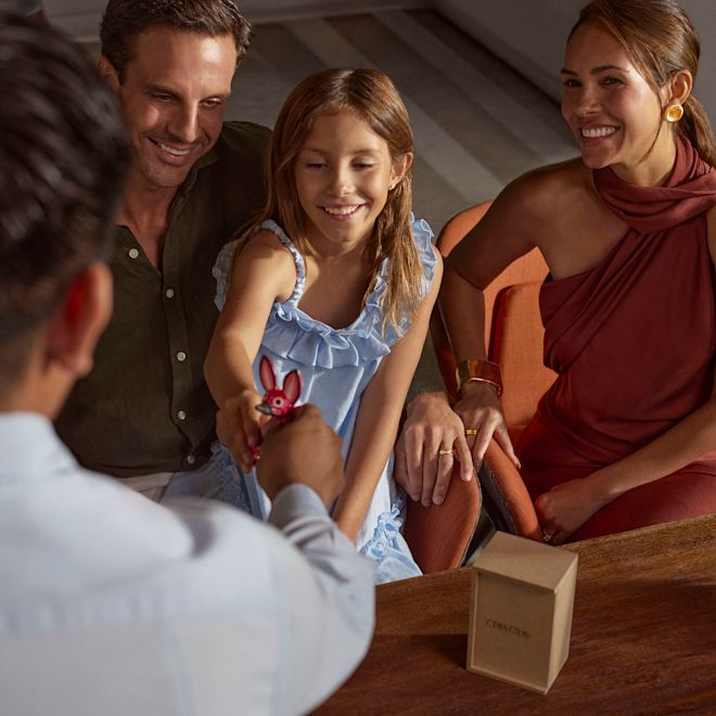 A teammember is gifting a small pink wooden animal toy figurine to a girl  while her parents watch on smiling.