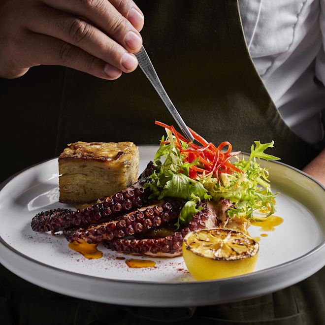 Chef Adăugând ultimele atingeri pe o farfurie cu caracatiță și legume la restaurantul Maratea