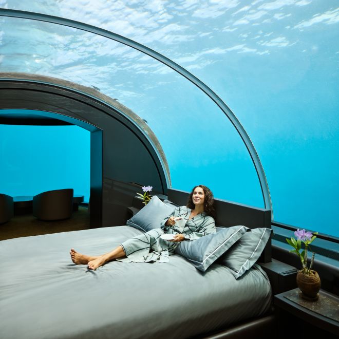 Woman relaxing on bed in underwater guest room. Fish can be seen through the glass ceiling