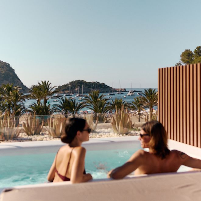 Zwei Personen entspannen sich im eigenen Swimmingpool mit Blick auf die Bucht und die Boote