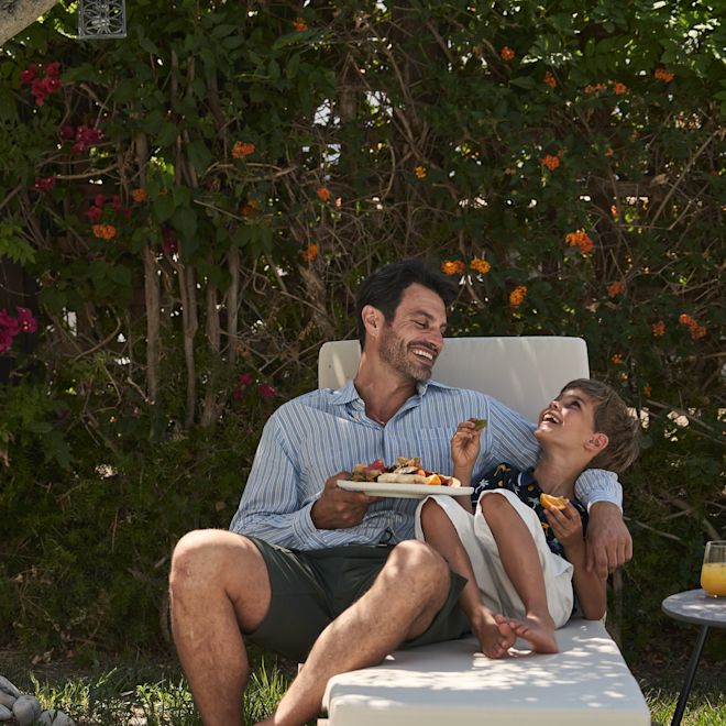 Man and Son Lying on a Lounge Chair, Laughing and Snacking