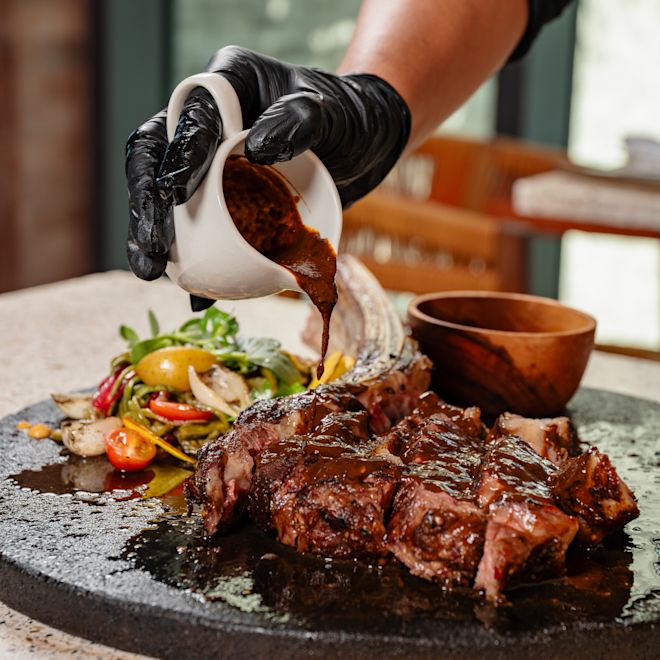 Chef Adding Sauce to a Plate with Meat at Maxal Restaurant