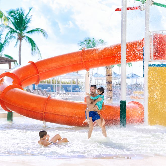 Dad with kids at water park, standing in wading pool in front of water slide.