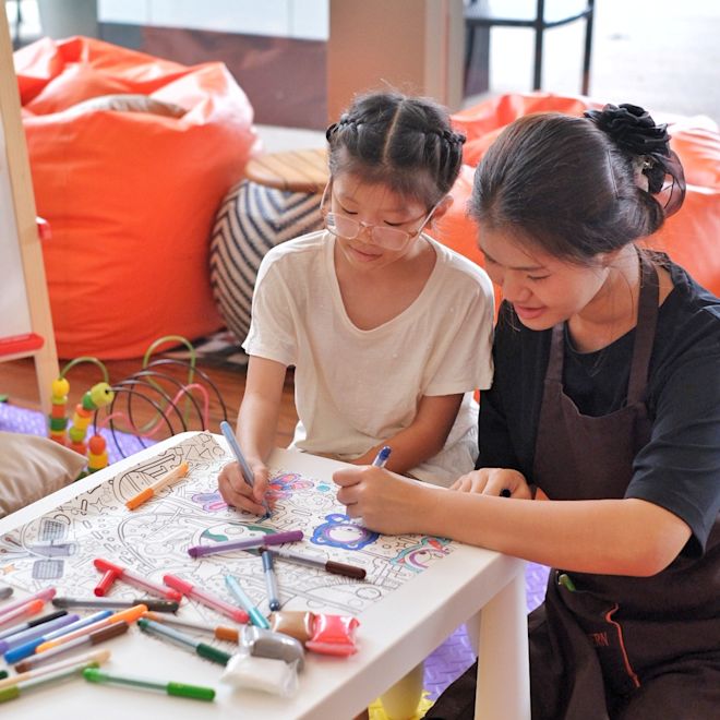小さなテーブルに座り、カラフルなペンで絵を描いている少女と女性