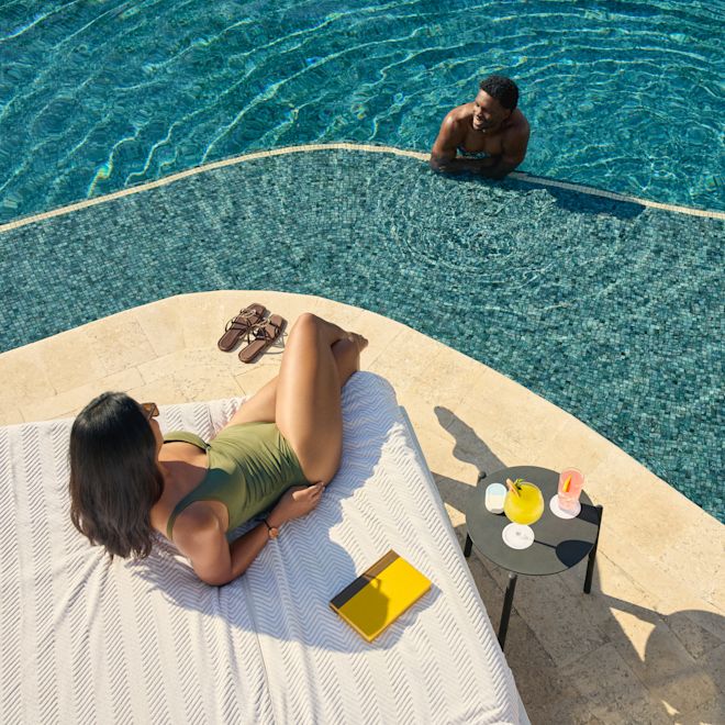 Femme se relaxant sur un transat près d'une piscine et parlant à un homme dans la piscine