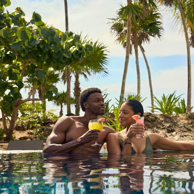 رجل وامرأة يسترخيان في حمام السباحة ويتناولان المشروبات