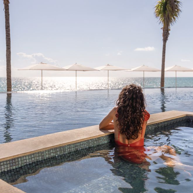 Woman looks out from pool towards ocean