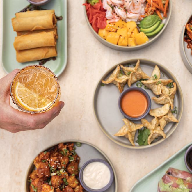 Hand, die ein Getränk über einem Tisch mit Speisen hält