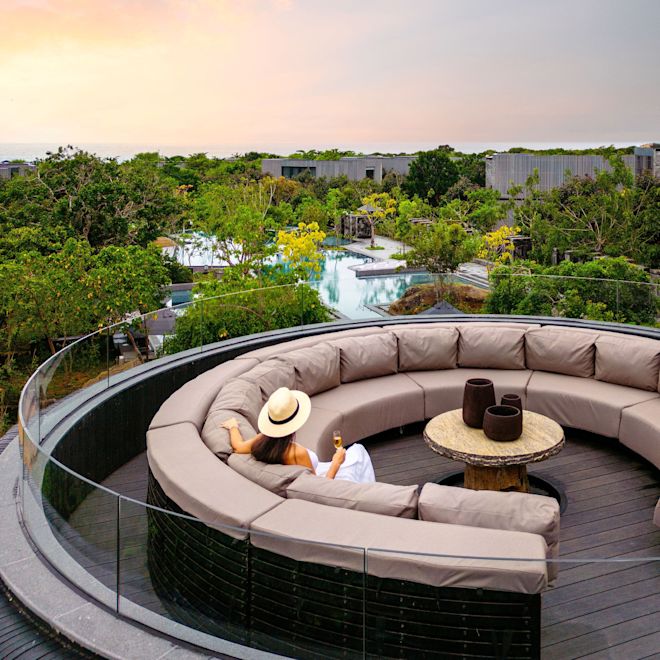 Mujer en área de estar al aire libre con vista a la piscina y al atardecer