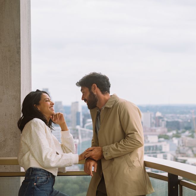 Hombre y mujer riendo mientras se paran en el balcón con vista a la ciudad