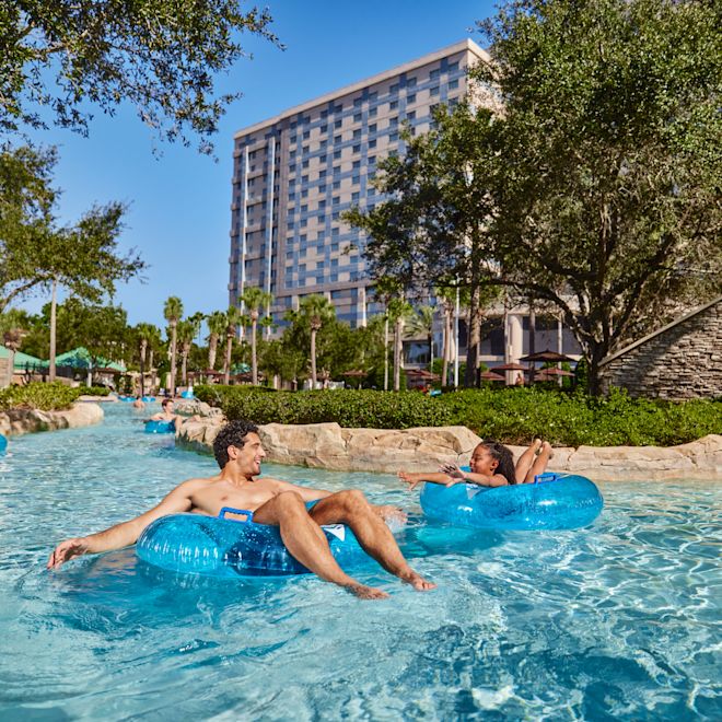 Pria dan gadis muda menggunakan tabung karet di area kolam renang luar ruangan