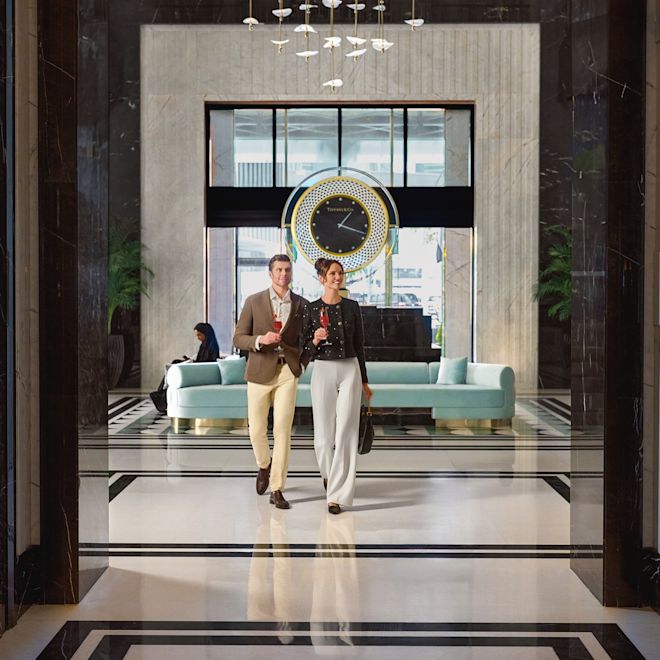 時計が飾られたホテルの廊下を歩く男女