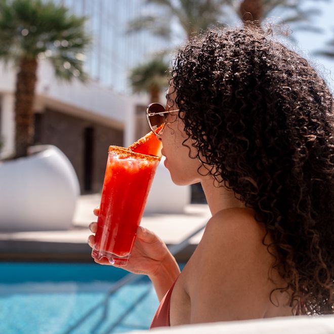 a Woman Having a Drink by the Outdoor Pool with Palm Trees in Background