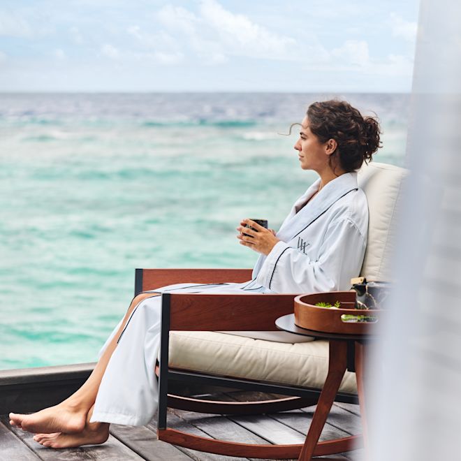 Femme se détendant à l'extérieur en buvant un verre et admirant la vue sur l'océan