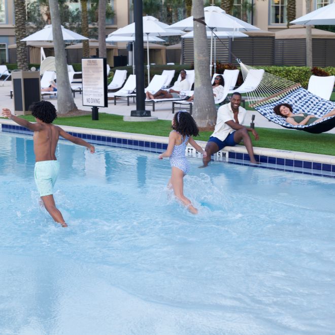 tamu yang duduk di tepi kolam renang, anak-anak bermain di kolam renang