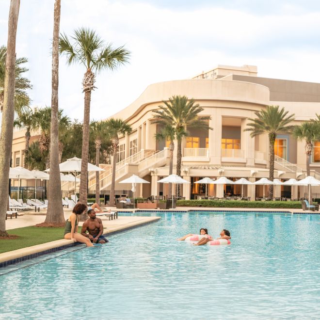 Area kolam renang luar ruangan dengan anak-anak mengambang di kolam renang sementara orang dewasa bersantai menonton