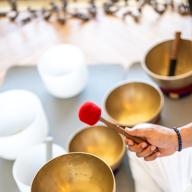 Person, die eine goldene Singschüssel mit Matten und drei der gleichen Schüsseln auf dem Tisch hält