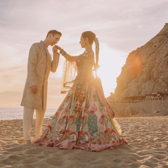 Un hombre besa la mano de una mujer en la playa al atardecer